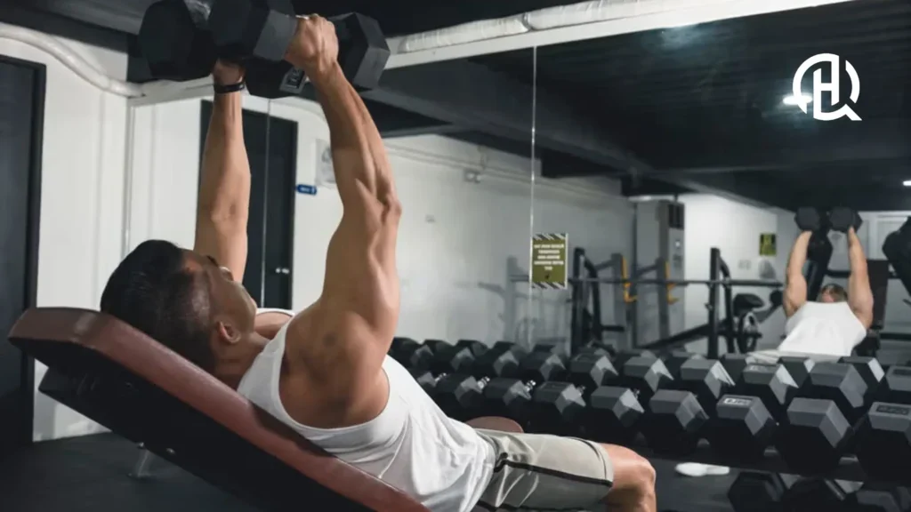 Man in a white tank top performing an incline dumbbell with a mirror reflection